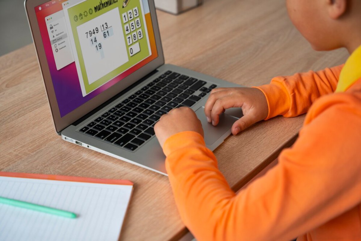 Child in orange shirt using a laptop with a mathematics interface on screen.