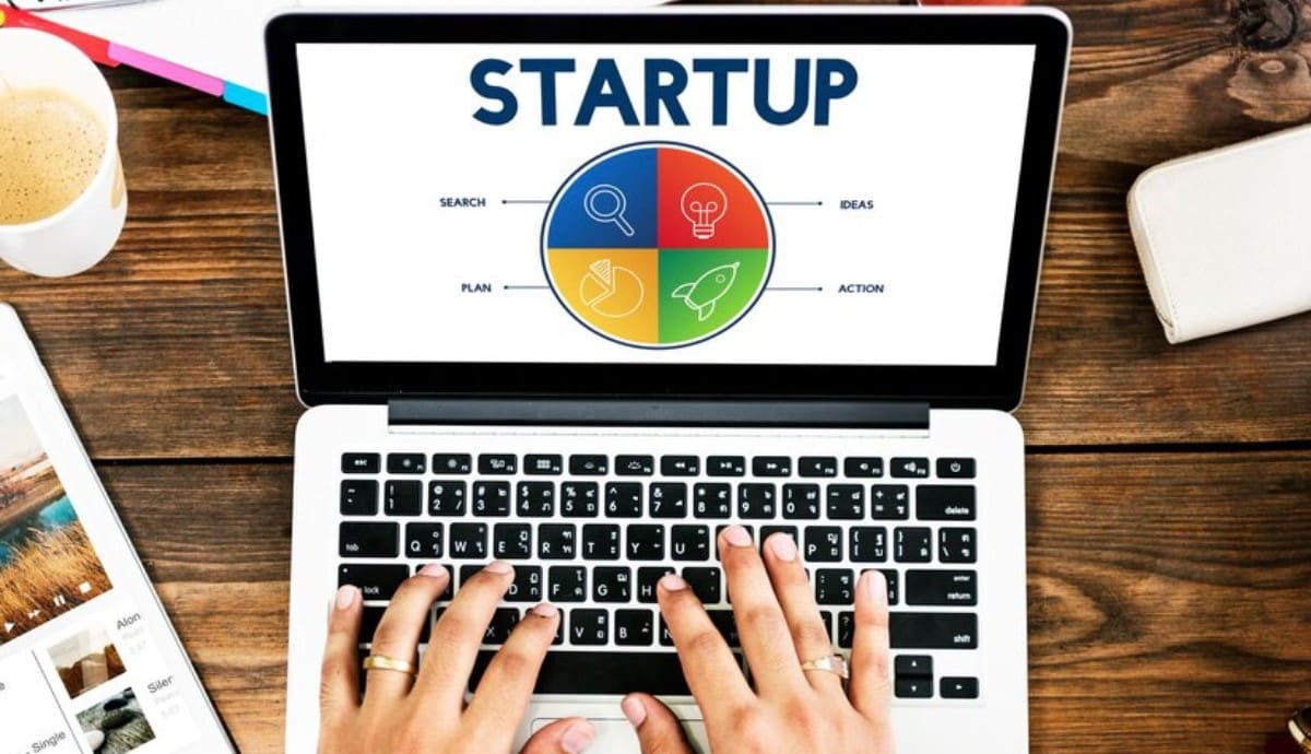 Person using a laptop displaying a colorful "STARTUP" strategy chart with icons.