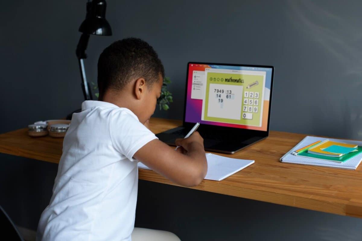 Young boy studying mathematics online at home with a laptop and taking notes.